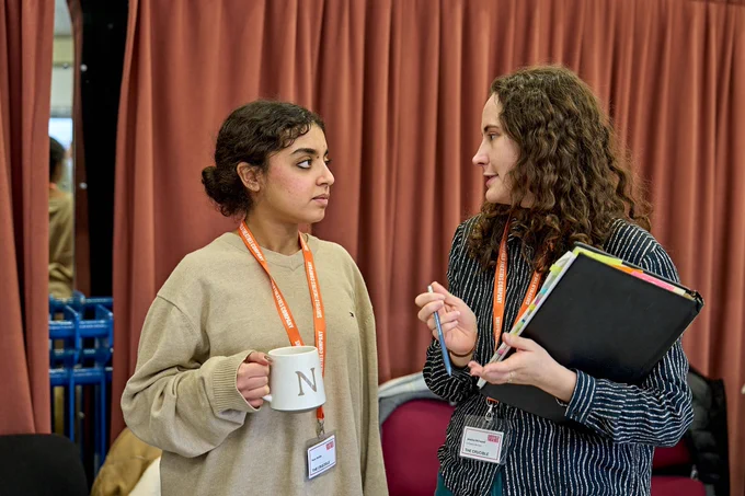 Two young women with dark hair talk to one another in a rehearsal room. Photo by Manuel Harlan.