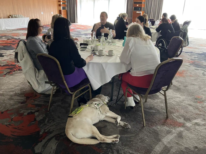 Group photo of people sitting around the table with guide dog Leon at his owner’s feet