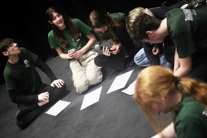 Young people sat on a floor with scripts.