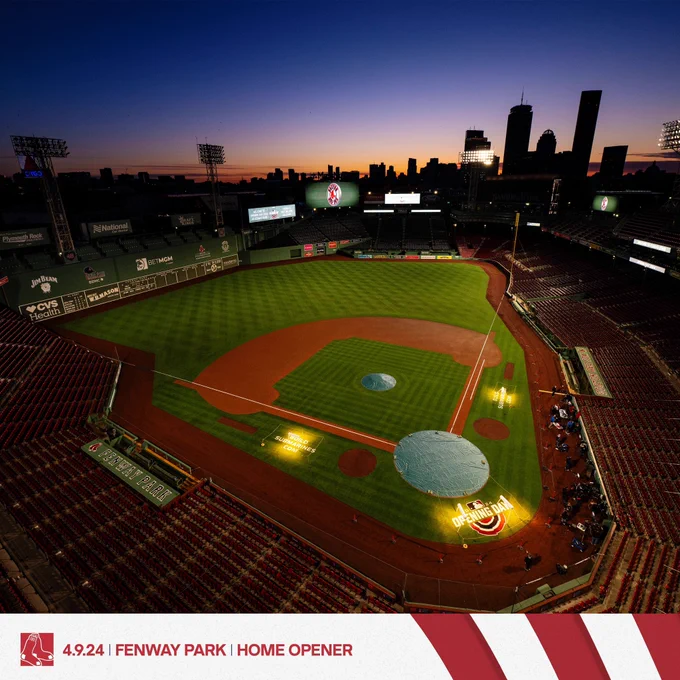 A wide shot of Fenway, taken from seats high up along the third base line, shows the purple and organize skies over Fenway as the sun rises over the Boston skyline just past the ballpark.