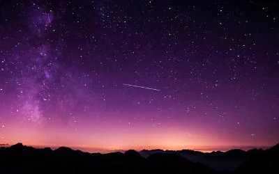 a photo of the night sky, with the landscape in darkness, with a pink and purple haze in the sky and with stars twinkling