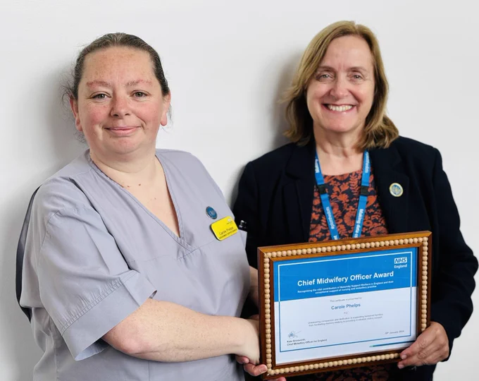 Two people stand together, one presenting a certificate to the other