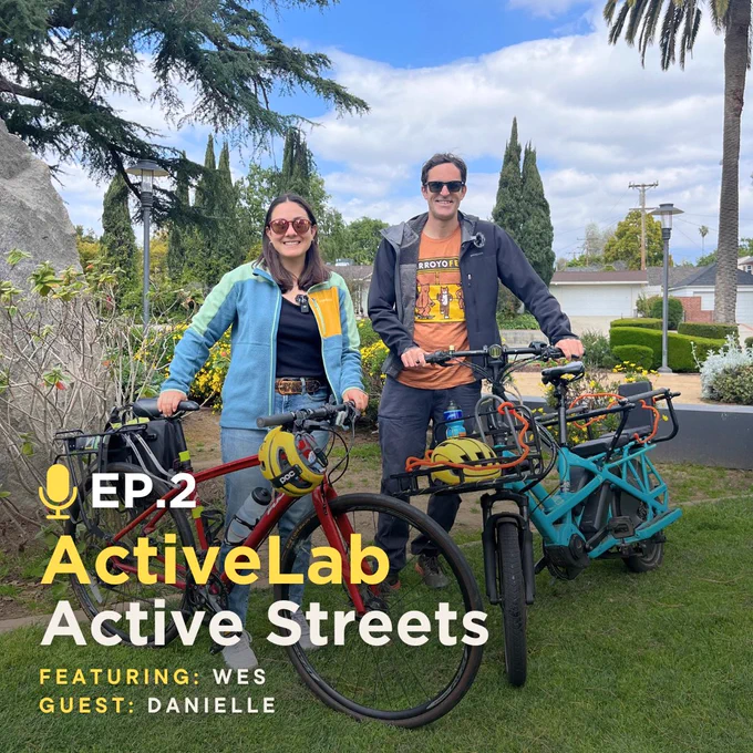 Two happy cyclists pose with their bikes in a public park during the day.
