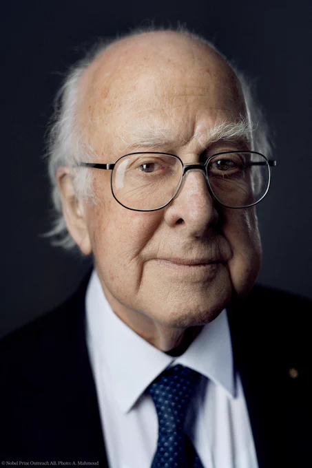 Official Nobel Prize portrait of Peter Higgs. He is wearing a dark suit and white shirt and a dark blue tie. 