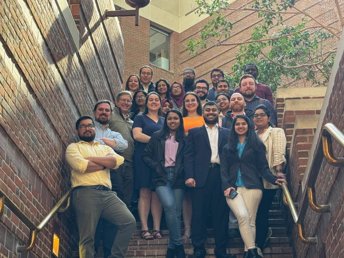 Members of MSU's inorganic chemistry specialty pose for a low-angle group photo on a brick stairway. Brass handrails flank the group, with a tree in the background.