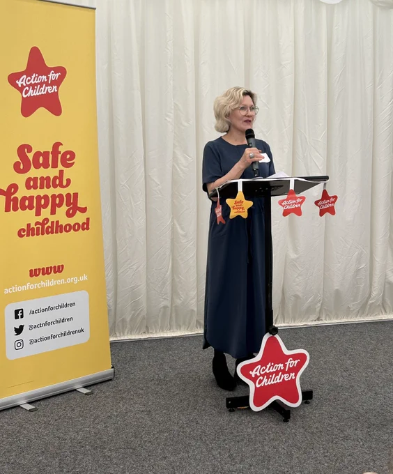 Image shows Action for Children NI Director Lorna speaking behind a podium. A pop up reading ‘Safe and happy childhood’ is on the left of screen.