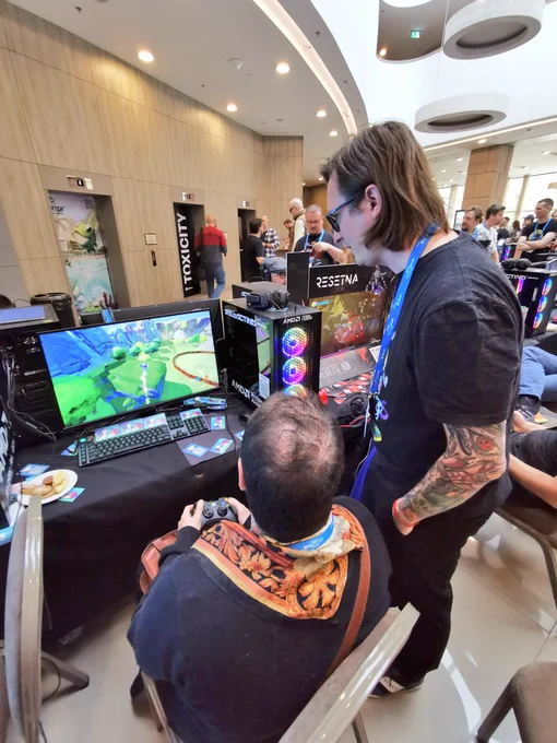 Photo of one person sitting down and playing Herdles, and another person standing next to them.