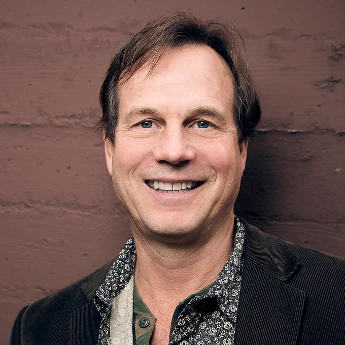 grey jacket. black and white shirt with floral pattern. short brown hair. grinning. pill paxton = a white dude.
