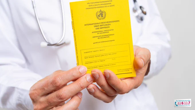 Foto eines Arztes mit einem gelben Impfbuch in der Hand, das er in die Kamera zeigt.
