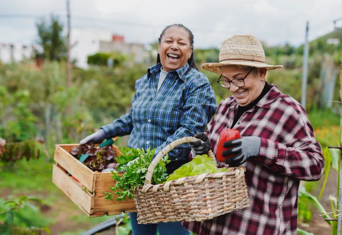 two seniors smiling holding baskets with harvested vegetables