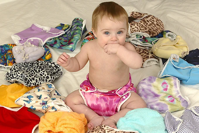A baby wearing a reusable nappy, surrounded by reusable nappies