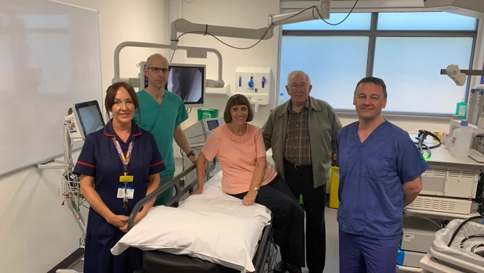 Jean, in a peach top, and Derek, in a green jacket and patterned shirt, are in the centre of the photo, with nurse Jill Effard, in navy, and fellow Alexander Seager in green to the left and Prof Colin Rees in mid-blue to the right.