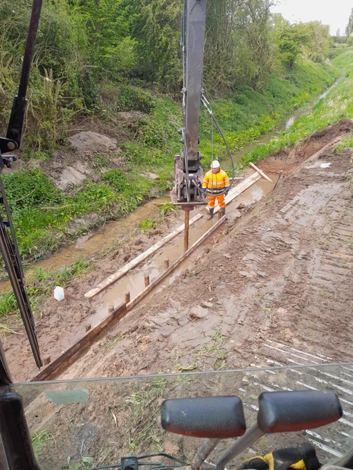 Operative stood in the watercourse while machine operates to repair bank slip