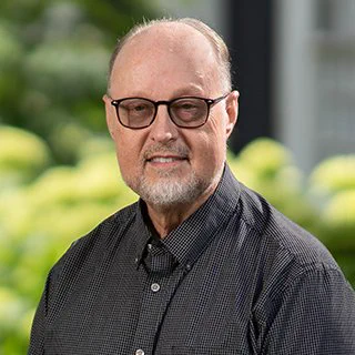 Photo of former Penn State librarian Paige Andrews wearing black-rim glasses and a dark button-up. He is standing outside and smiling