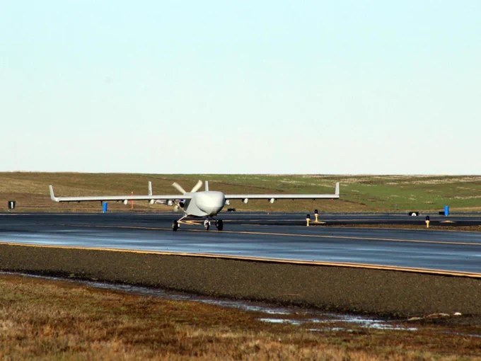 An uncrewed aerial system on a runway with a field behind it