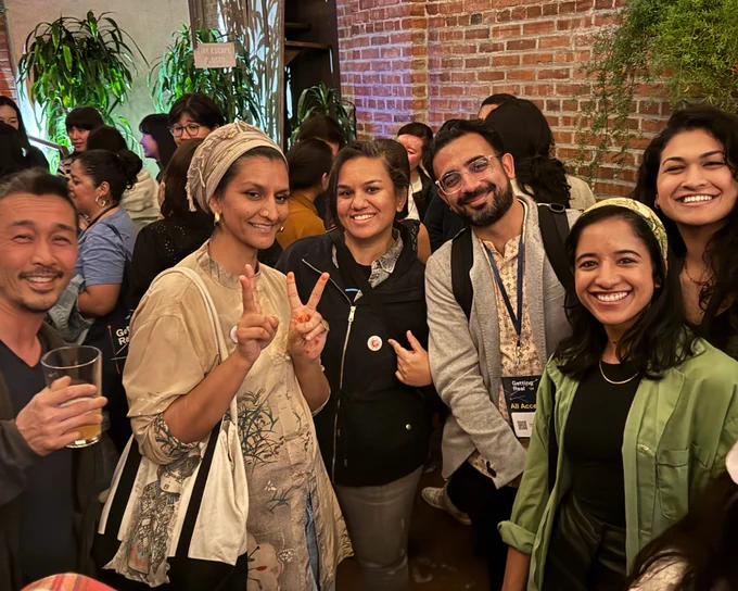 At the BGDM/A-Doc meetup, six people of color smile for a photo in a crowded room.
