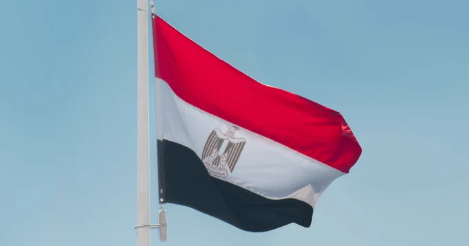 The flag of Egypt flying in the wind under a blue sky. 