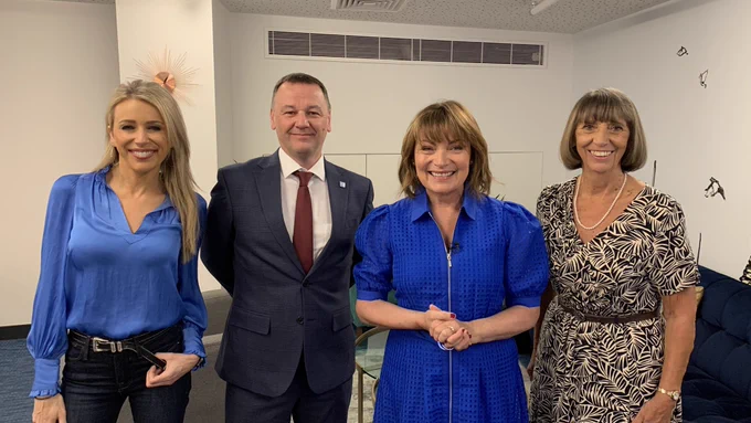 Lara is on the left and wears blue, Prof Rees is in a navy suit and white tie, Lorraine wears a blue dress and Jean is in a black and white dress. They are in a room with white walls and blue floor and furniture.