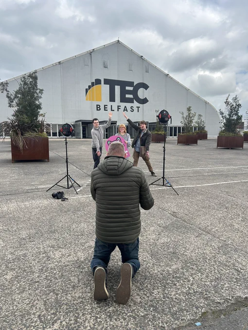 Photo of 3 NOW Group team members having their picture taken by a photographer in front of the Titanic Exhibition Centre in Belfast.