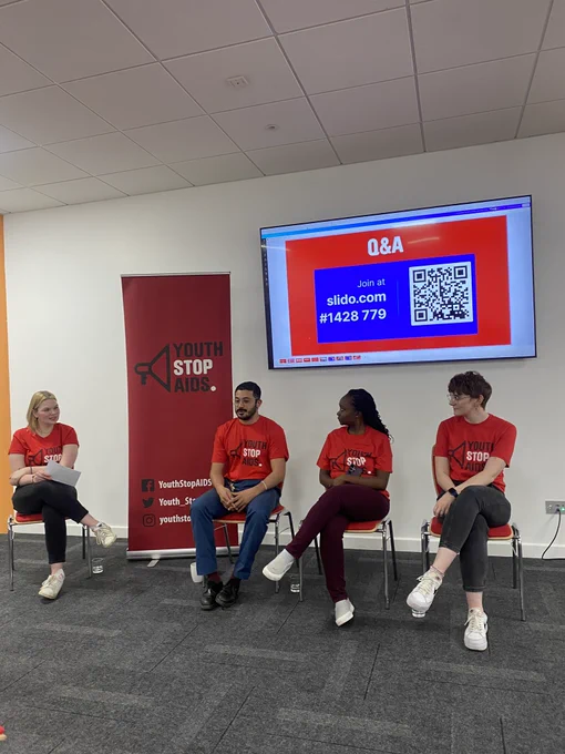 4 people sit in from of a screen and banner.
