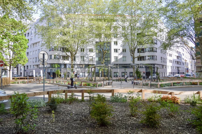 People walk, cycle, and sit in a “Super Island” in Lyon— an intersection transformed into a public space by introducing traffic calming, trees and plants, street furniture, and bike parking.