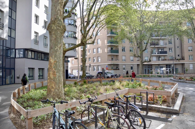 People walk, cycle, and sit in a “Super Island” in Lyon— an intersection transformed into a public space by introducing traffic calming, trees and plants, street furniture, and bike parking.
