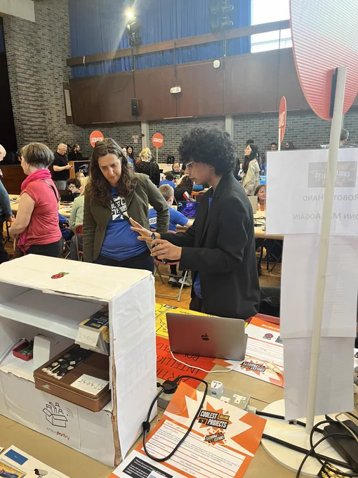 A judge from the Raspberry Pi Foundation giving feedback to a young creator on their project at a table filled with projects