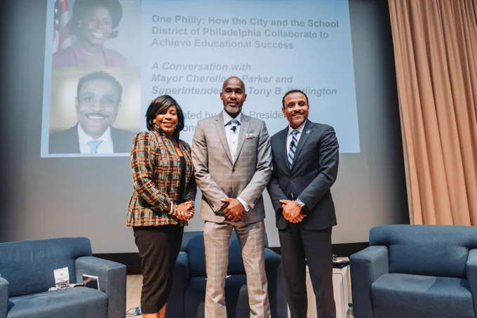 Three people pose for a photo and smile at the camera. There is a screen behind them displaying details of the session.