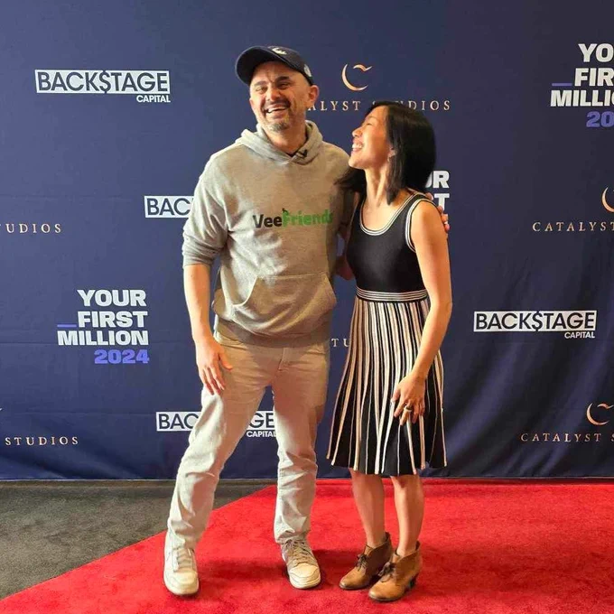 Gary Vee and Tiffany laughing in front of a black Your First Million Live step and repeat