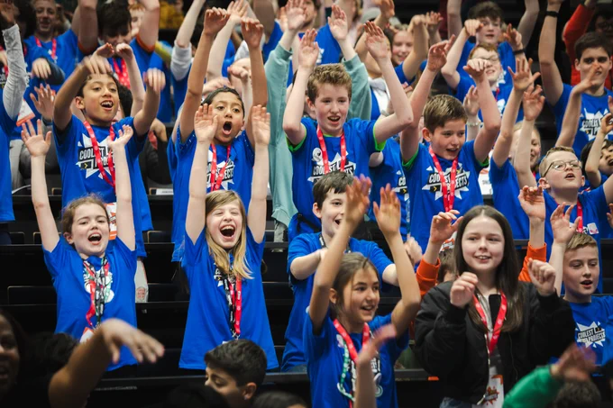 Lots of young creators in their blue Coolest Projects t shirts raising their arms in the air.