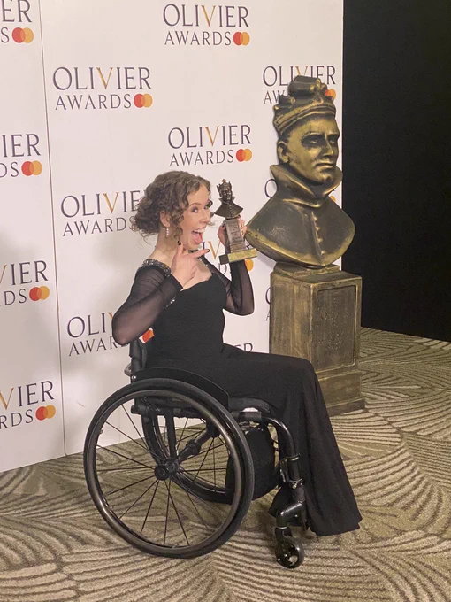 A photo showing a performer in a black dress holding a statuette, pointing with her other hand