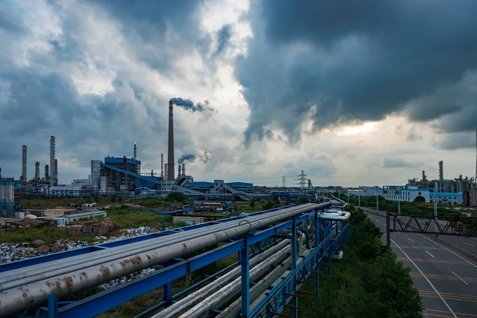 A chemical plant producing pollution next to a highway with a pipeline running alongside it