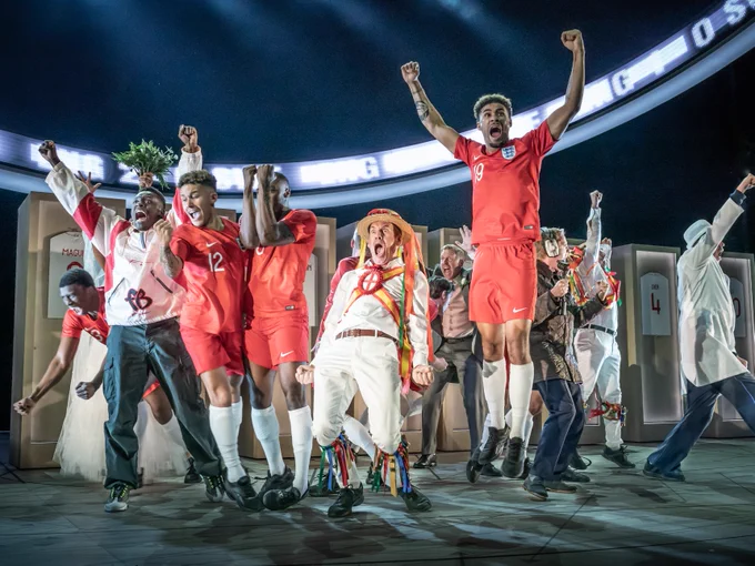 A group of men in red england football kit and a man in a maypole dancing kit jump and shout in victory.