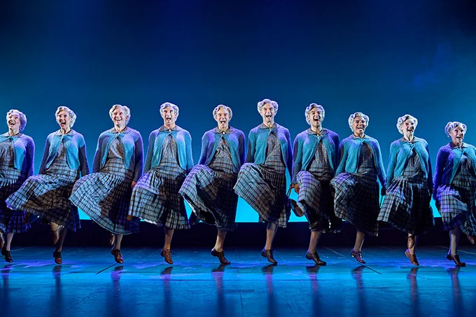 A photo showing a group of performers dressed as old women dancing in a line on stage