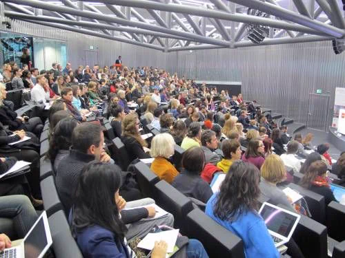 An upper view of a classroom with stadium seating at the Geneva law school. The room is filled with students, some holding laptops or notebooks.