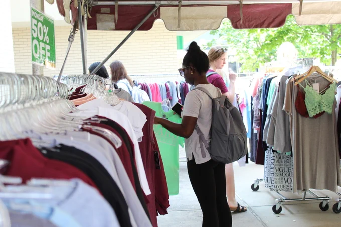 Girl shopping through racks, holding a green t-shirt at the Tent Sale 