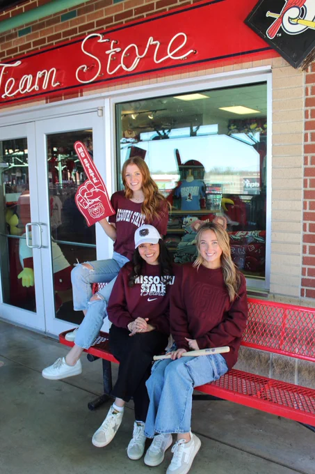 3 girl students in maroon Bear Wear sitting in front of the Team Store at the baseball stadium 