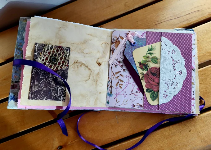 A small handmade journal opened to a page that shows pockets, tags, and lace.