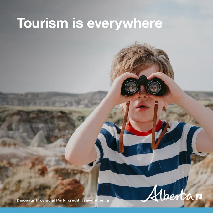A child looking through a pair of binoculars. Text reads Tourism is everywhere. Photo credit in the bottom left corner: Dinosaur Provincial Park, Travel Alberta. The Alberta government logo is in the bottom right corner. 