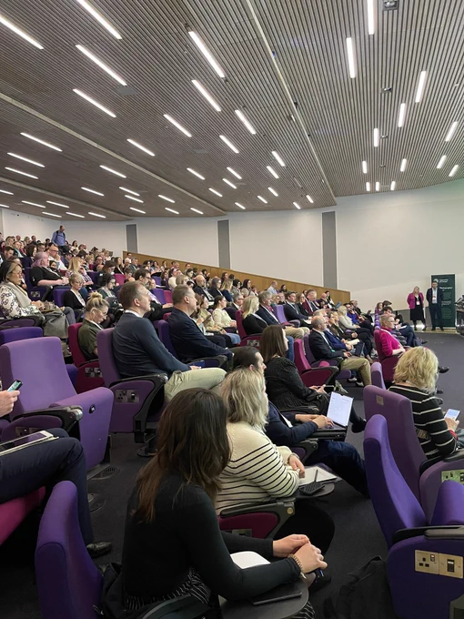 Full auditorium of people sat looking on to a stage