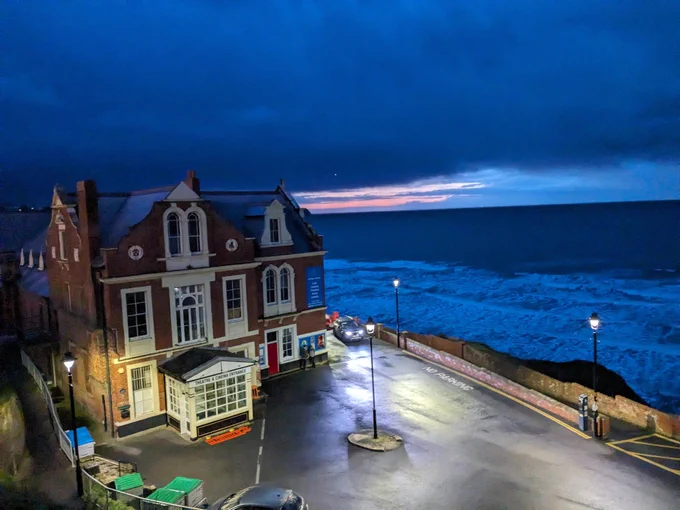 Whitby Pavilion lit by street lamps standing overlooking a stormy sea
