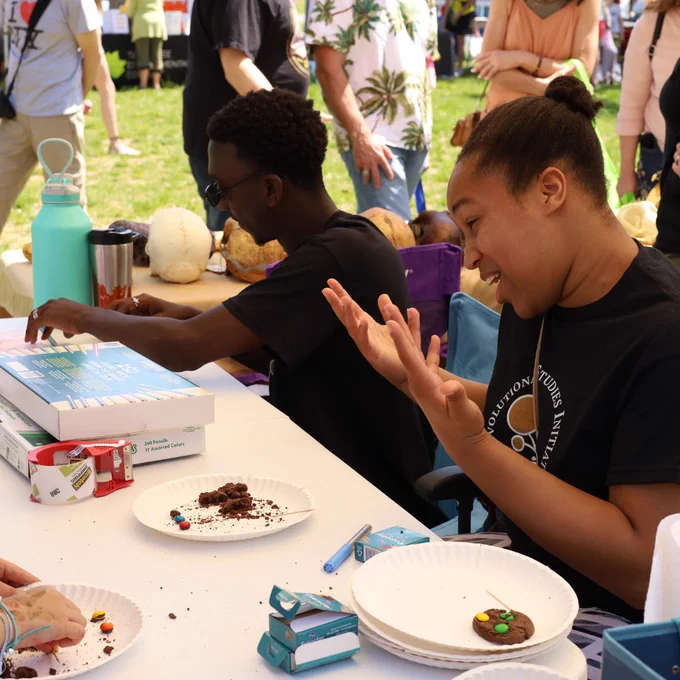 Two people sit behind a table showing children how to dig for candies in cookies - like excavating fossils!