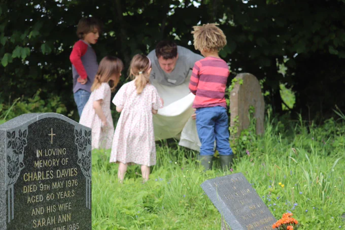four children and one adult looking for insects with a white sheet in a churchyard