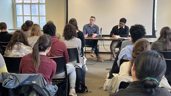 Ezra Klein sits at the front of a class while presenting to students.