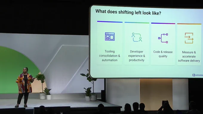Scaled out photo of Ajuna presenting on stage with a large screen behind her.