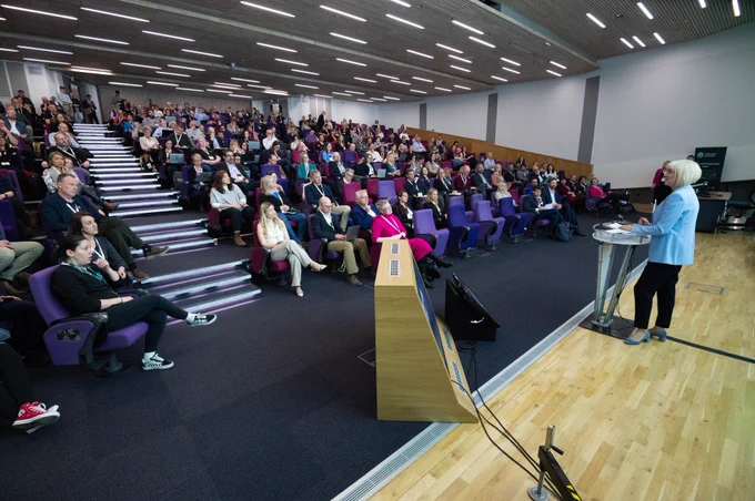 Full auditorium of people looking towards the stage listening to a speaker.
