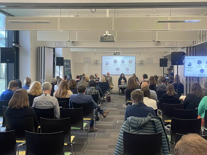 People sat looking toward a panel of speakers