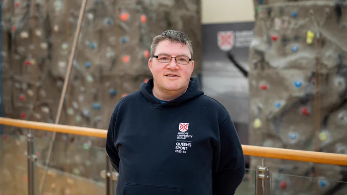 Richard Collis, supported by Orchardville, pictured in front of the climbing wall in Queen's Sport Physical Education Centre, 2024.
