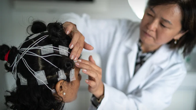 Image of Asian female doctor placing an EEG electrode on a patients head. (Getty Images)