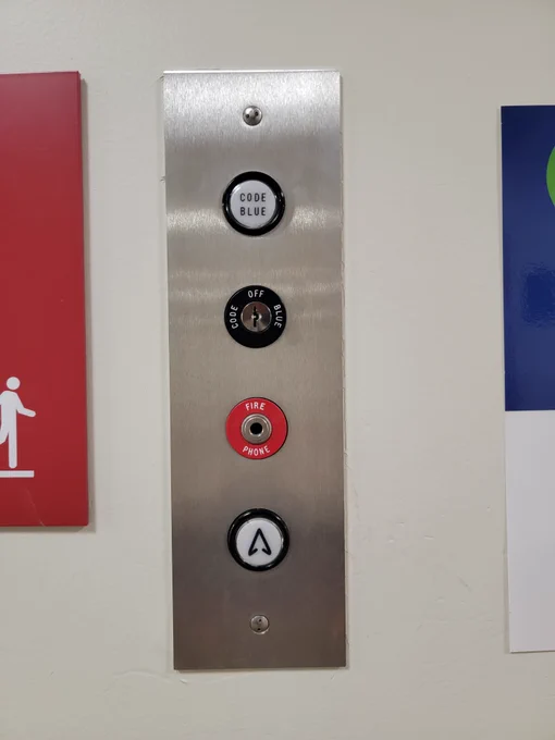 Elevator call button with Code Blue at top and up arrow at bottom